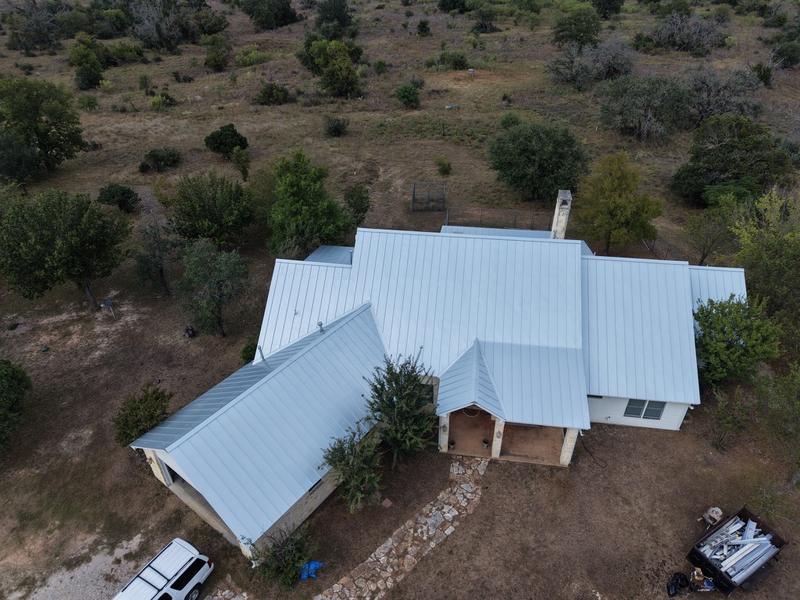 Overhead drone view of a finished light gray standing-seam metal roof on a rural home
